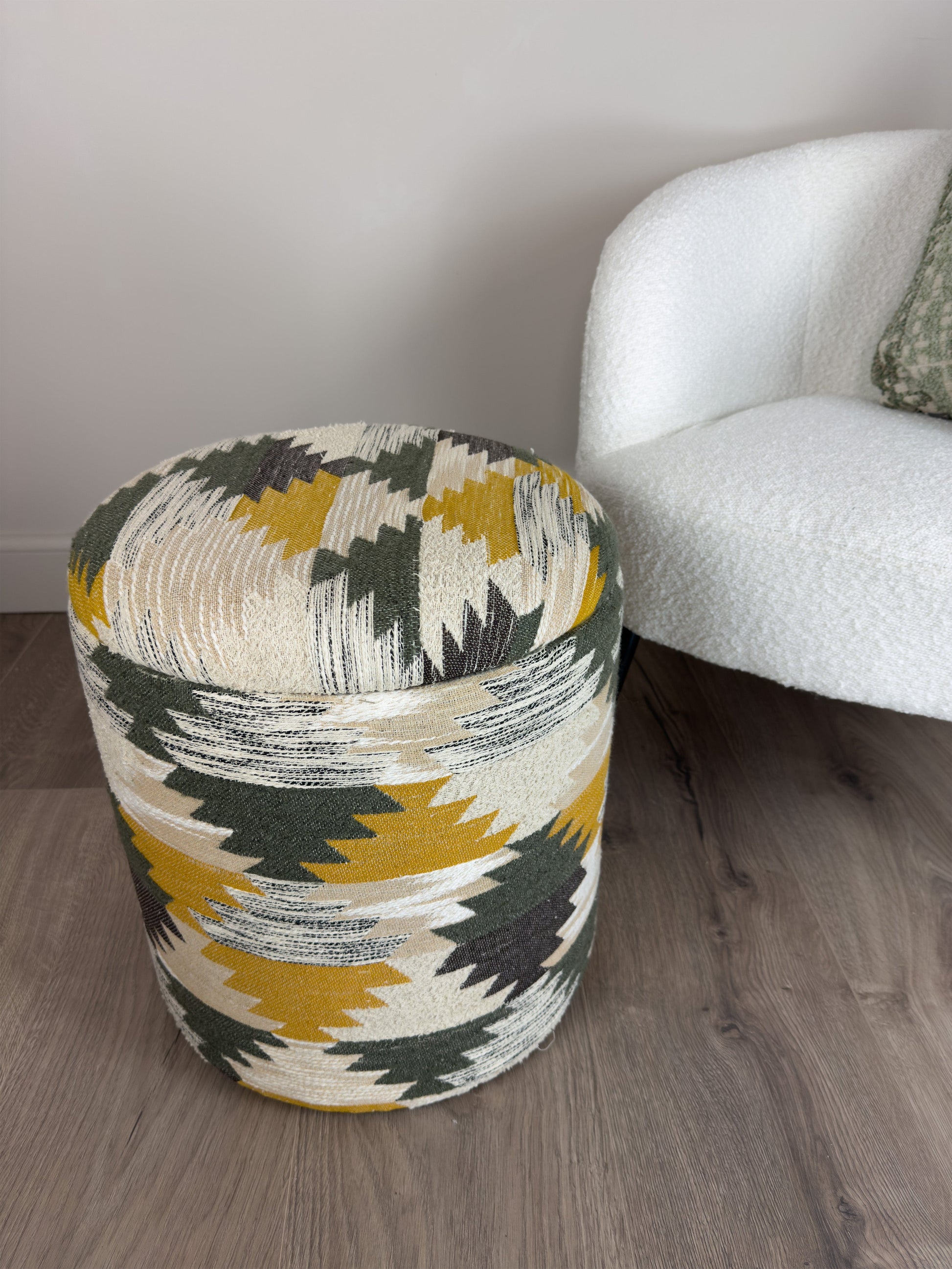 Patterned ottoman next to a white armchair on a wooden floor.
