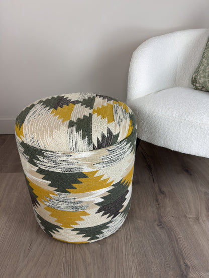 Patterned ottoman next to a white armchair on a wooden floor.