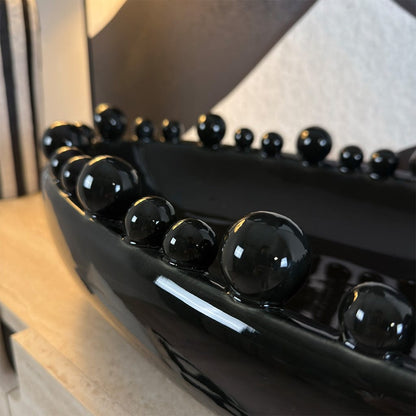 Close-up of a black oven handle with decorative black beads on a blurred kitchen background