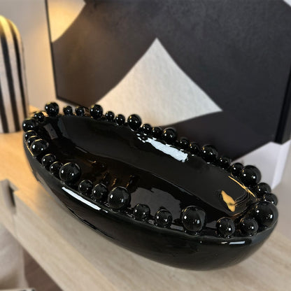 Black ceramic bowl with beaded design on a wooden surface