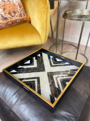 Decorative tray with abstract black and gold esign on a sofa