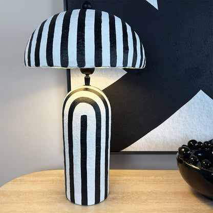 Black and white striped table lamp on a wooden surface with abstract art in the background