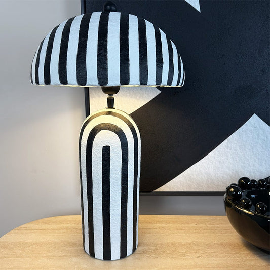 Black and white striped table lamp on a wooden surface with abstract art in the background