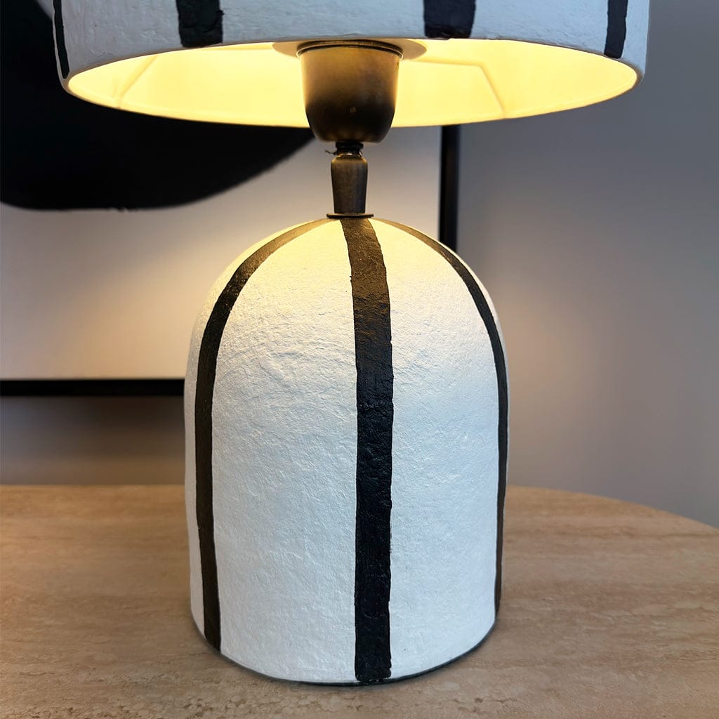 Table lamp with white base and black stripes on a wooden surface.