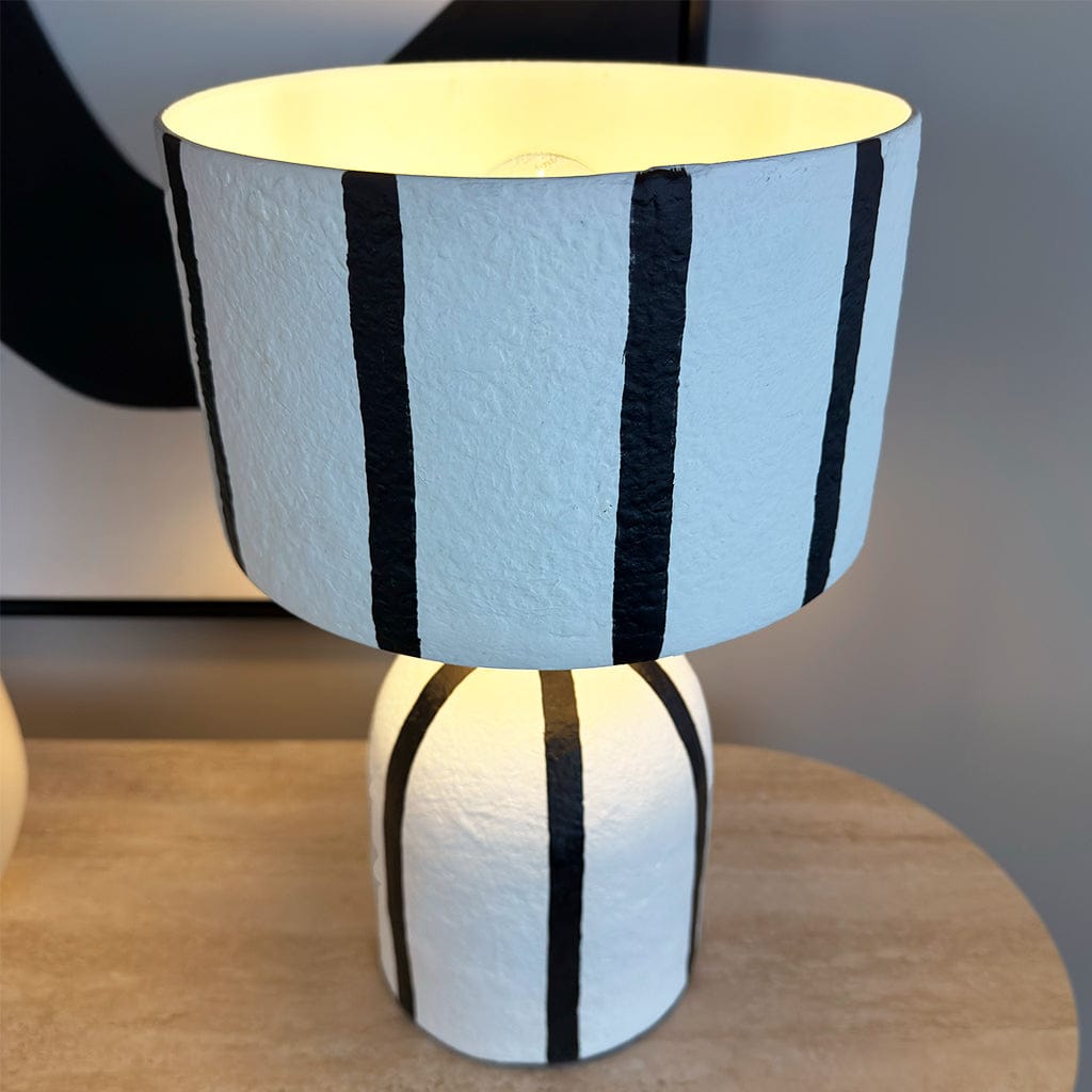 Table lamp with black and white striped design on a wooden surface.