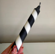 Black and white striped candle held by a hand against a plain background