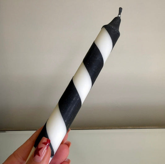 Black and white striped candle held by a hand against a plain background