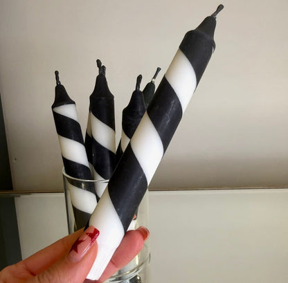 Black and white striped candles held by a hand with red nail polish.