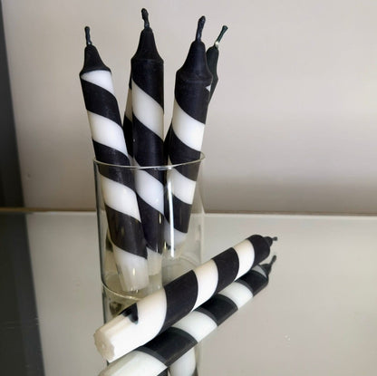 Black and white striped candles in a glass holder on a reflective surface.