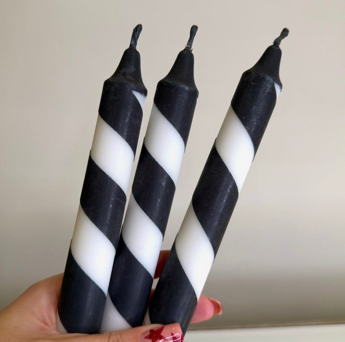 Three black and white striped candles held by a hand against a plain background