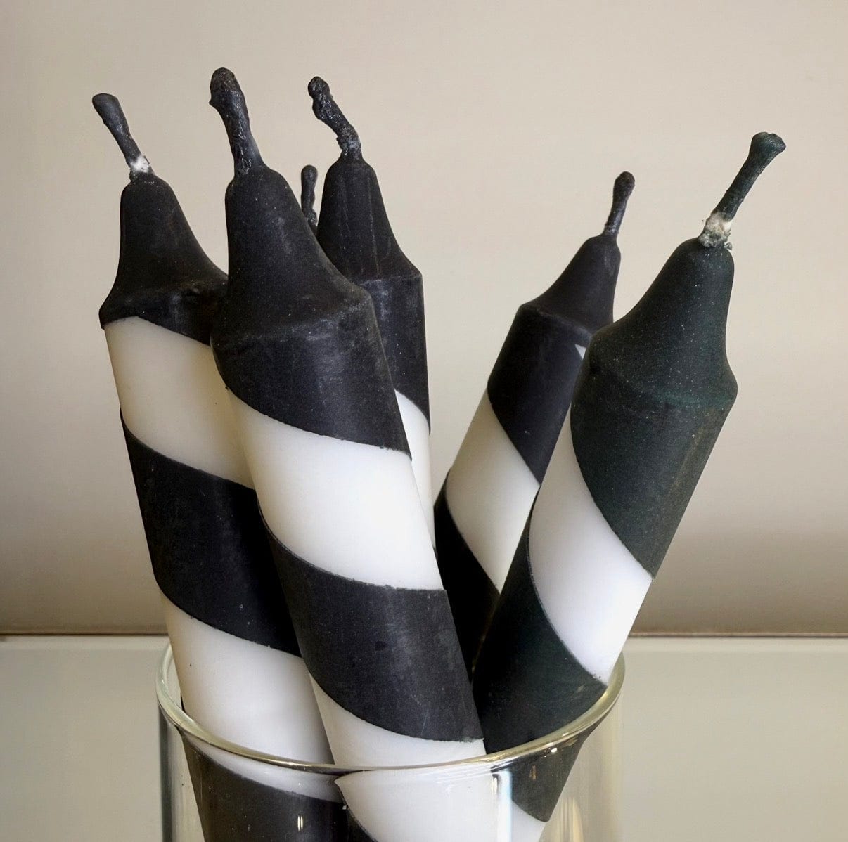 Black and white striped candles in a glass holder against a plain background