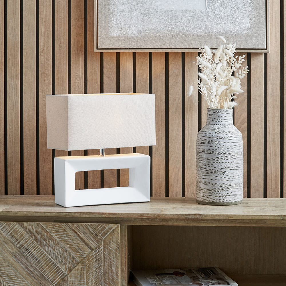 White table lamp and textured vase on a wooden surface with a wooden panel background