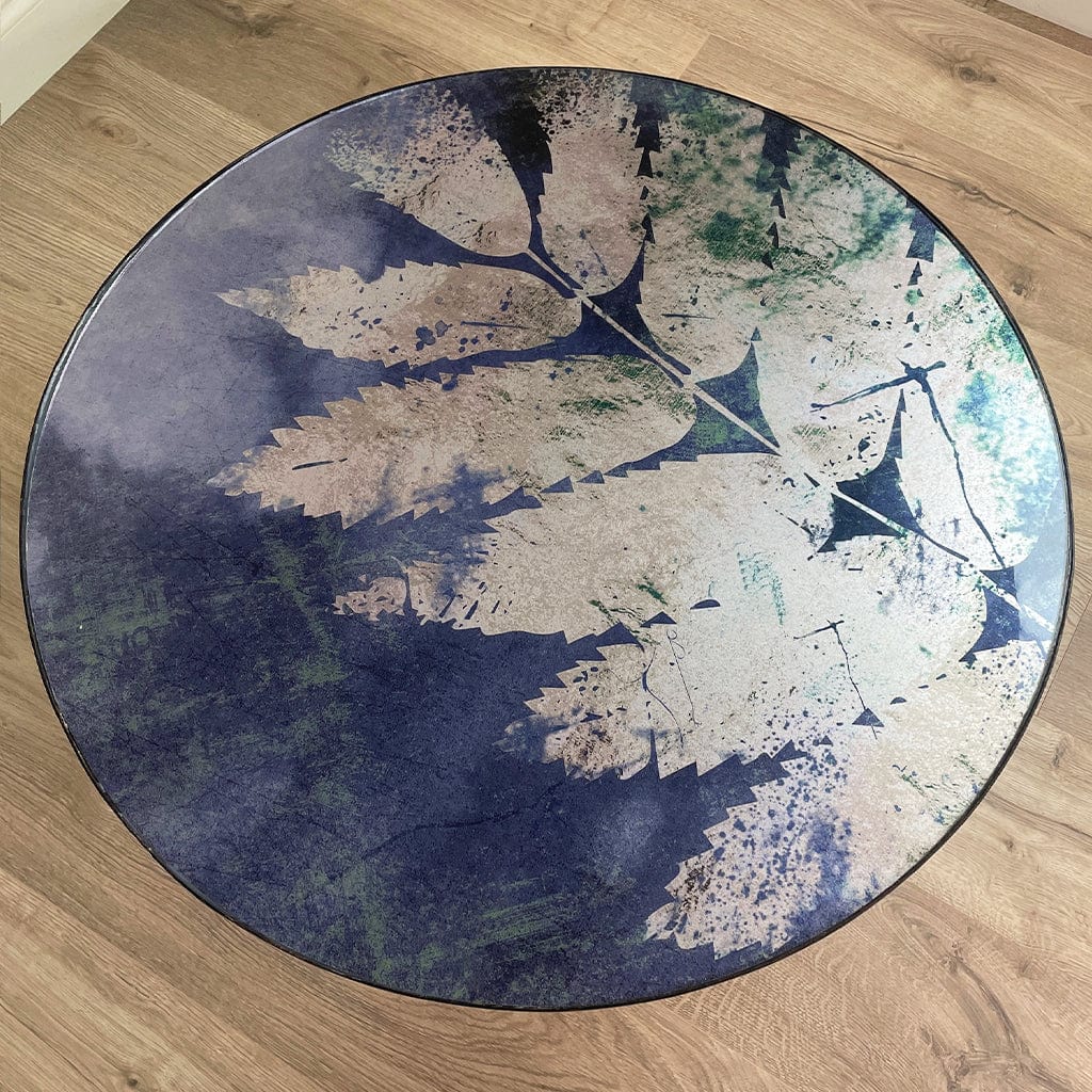 Round glass top table in blue with a silver leaf pattern on a wooden floor