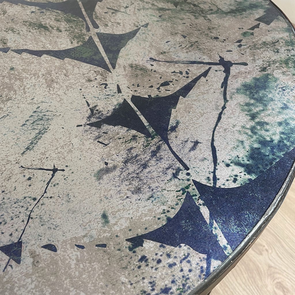 Round table with a textured surface featuring abstract blue and silver shapes on a light wood floor.