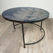 Round glass blue and pinky silver table with leaf-patterned top on a wooden floor