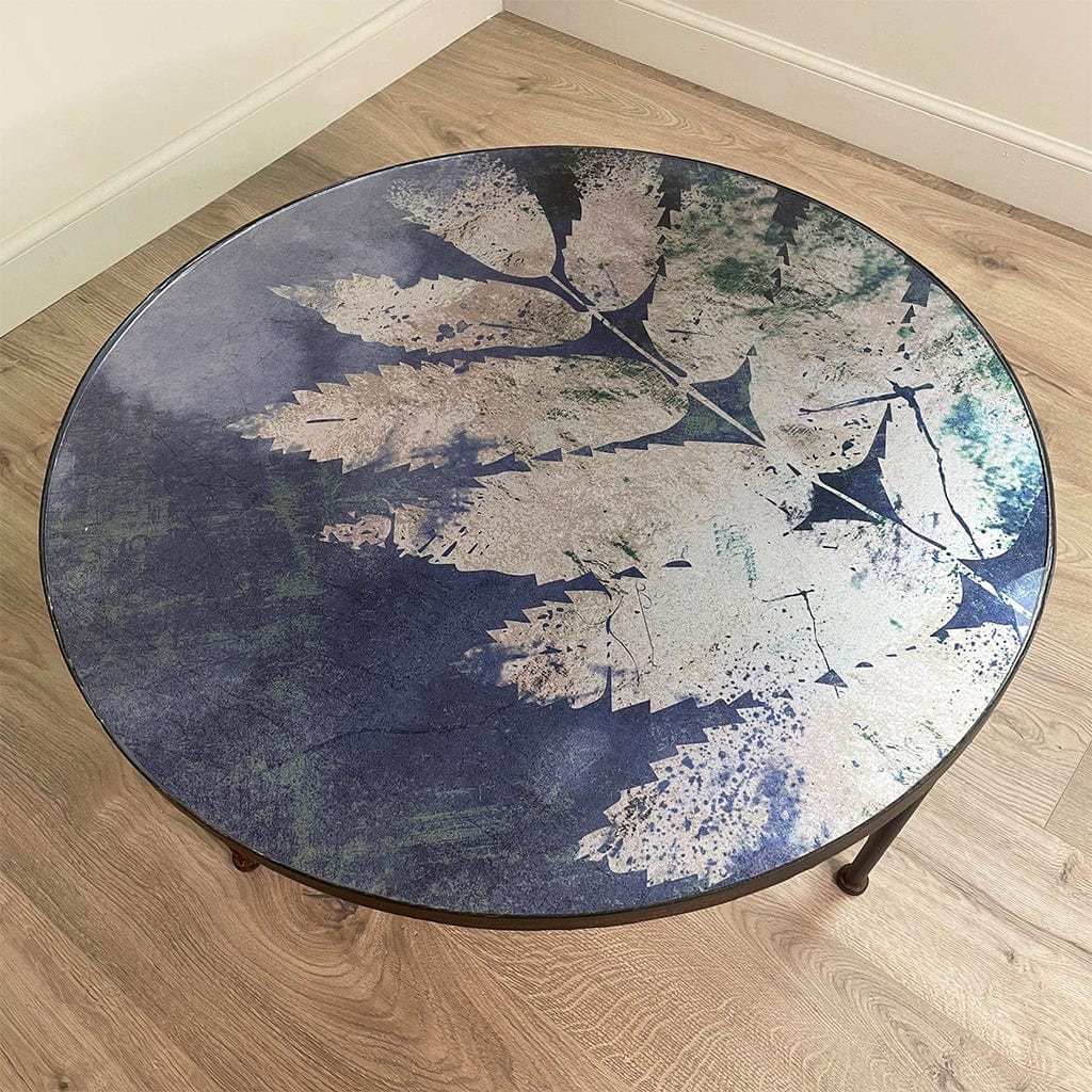 Round table with a leaf-patterned glass top on a wooden floor