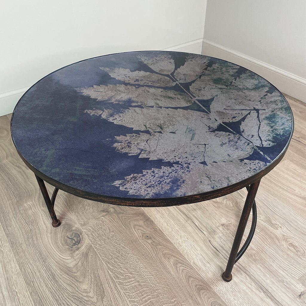 Round coffee table with a blue and gray leaf-patterned top on a wooden floor.