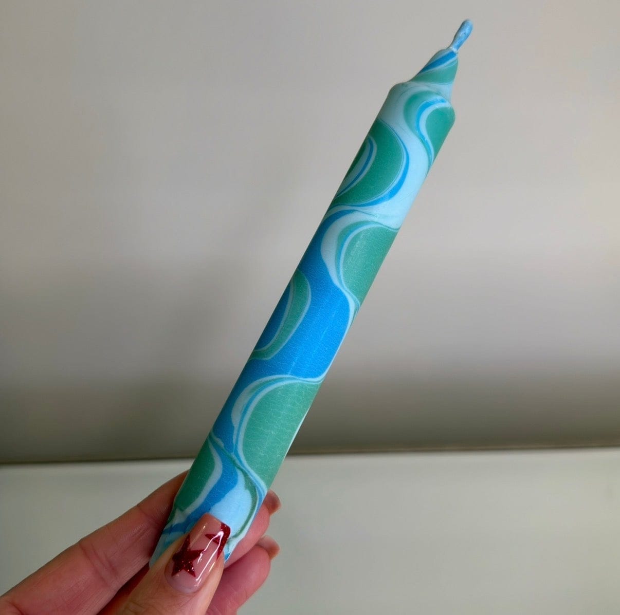 Hand holding a blue and green swirled candle against a plain background