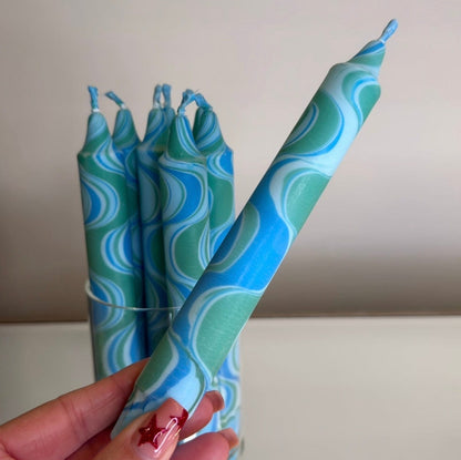 Blue and green patterned candles held by a hand against a neutral background