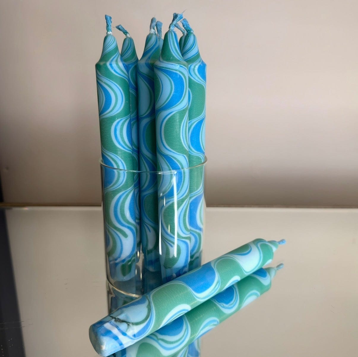 Three blue and green patterned candles in a clear holder on a neutral background