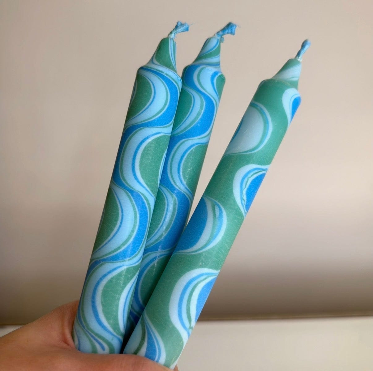 Three green and blue patterned candles held against a neutral background