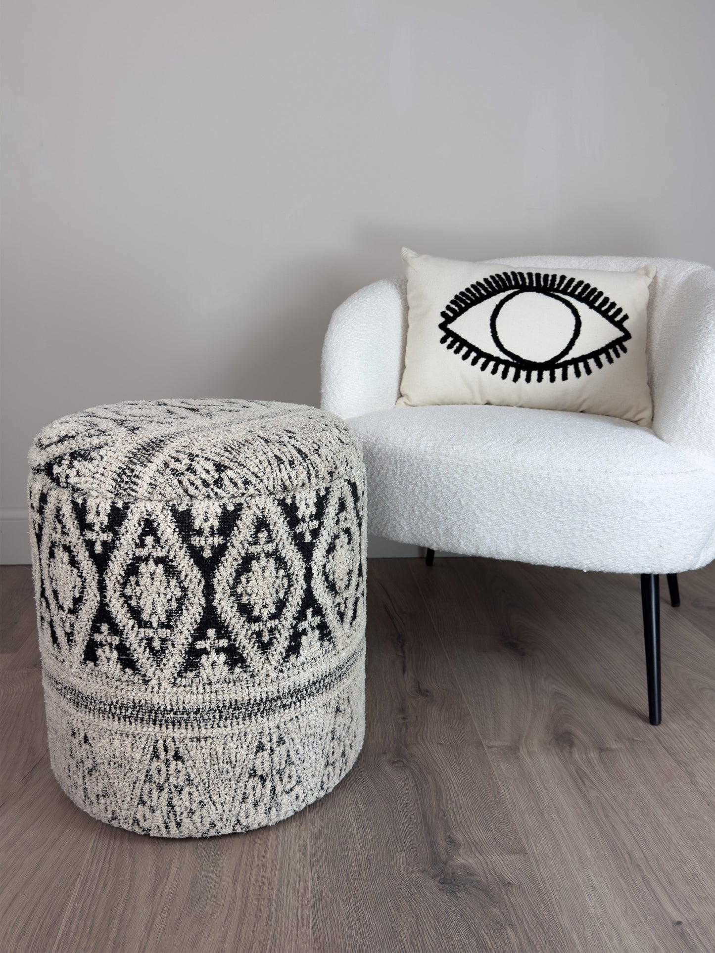 Patterned ottoman and white chair with eye design pillow on a wooden floor.