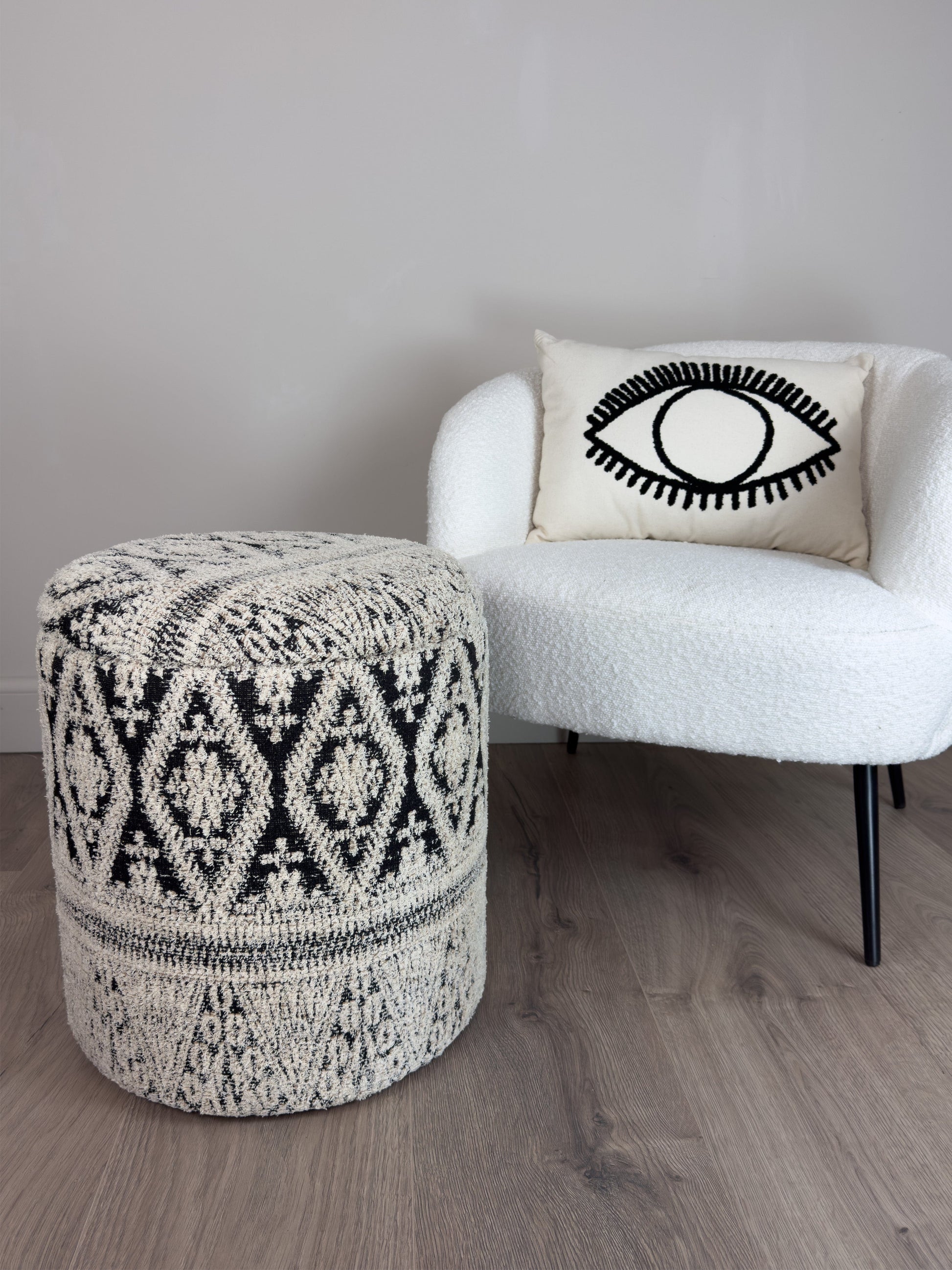 Patterned ottoman and white chair with eye design pillow on a wooden floor.