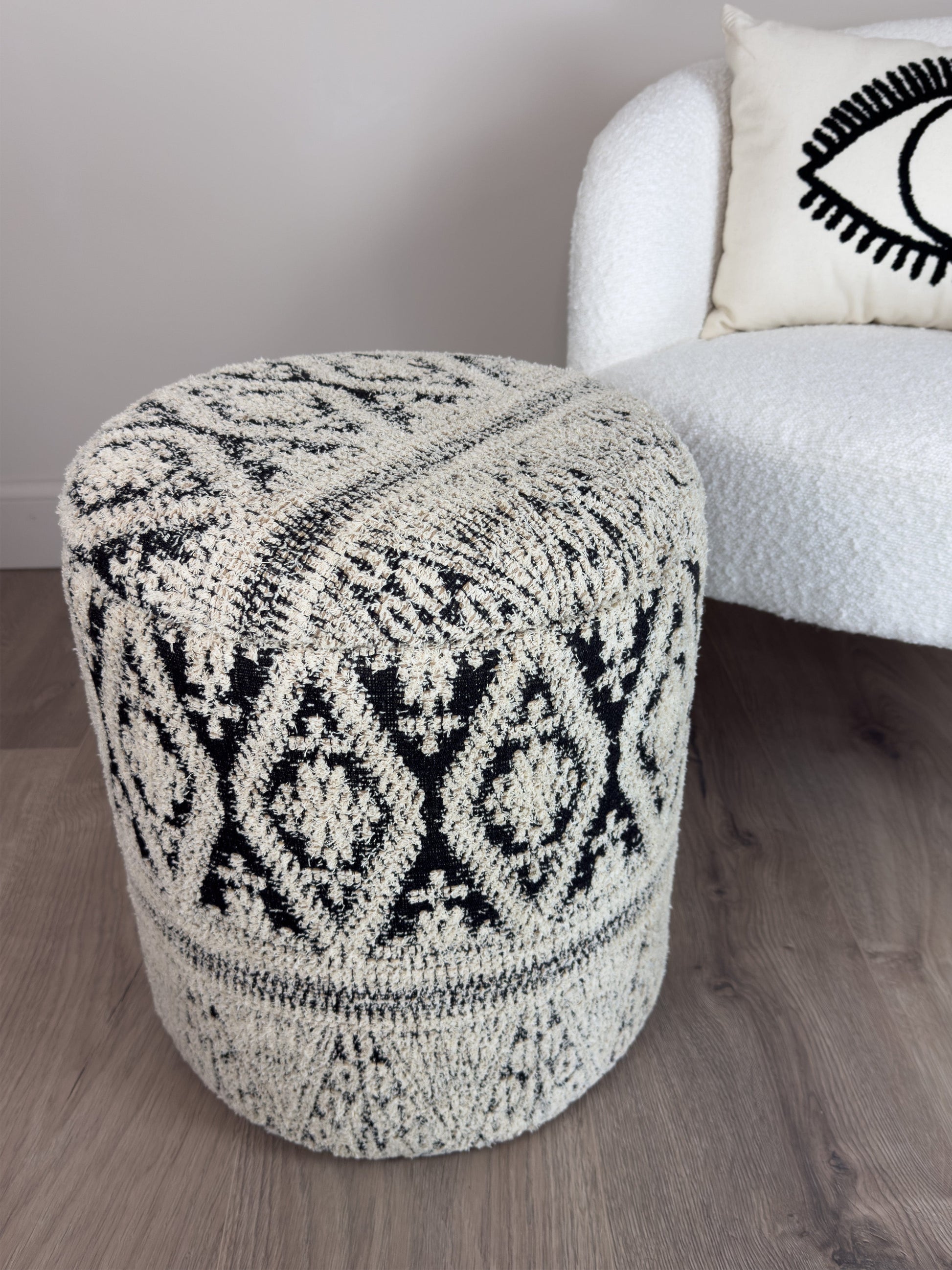 Patterned ottoman in a living room setting with a white armchair and decorative pillow.