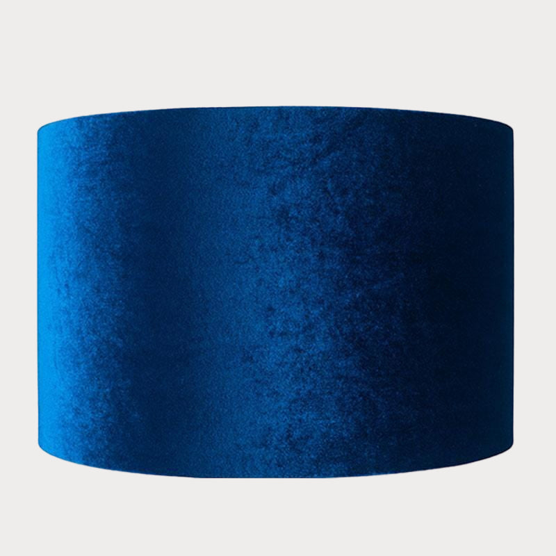 A cylindrical velvet lampshade in sapphire blue color with a bronze lining, displayed against a plain background.