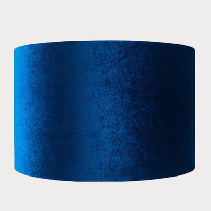 A cylindrical velvet lampshade in sapphire blue color with a bronze lining, displayed against a plain background.