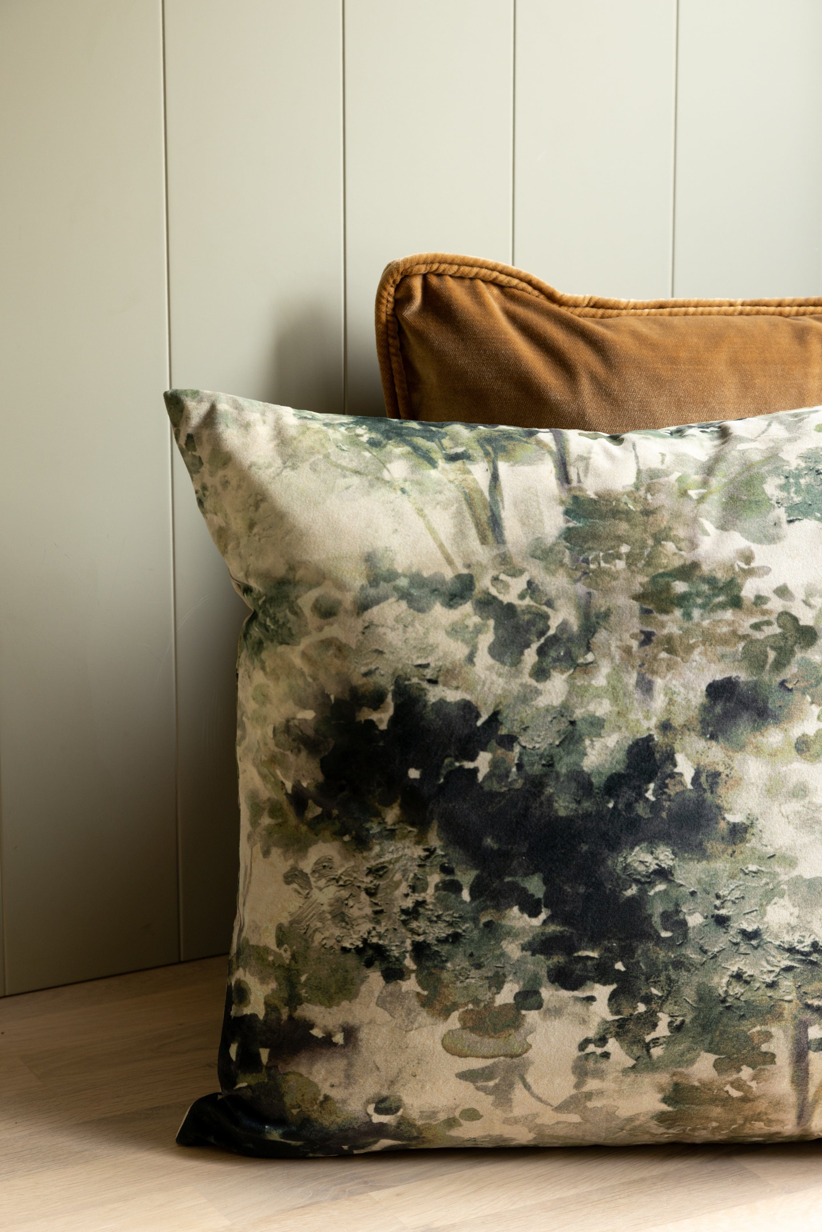 Decorative pillow with a watercolor pattern on a wooden floor against a neutral wall.