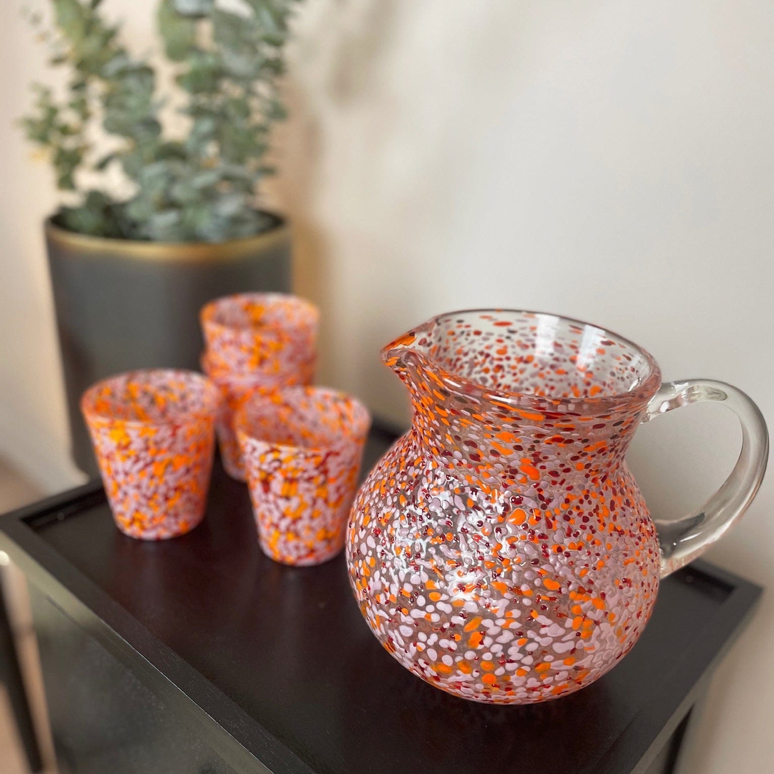 Set of orange and silver speckled glassware on a dark surface with a plant in the background.