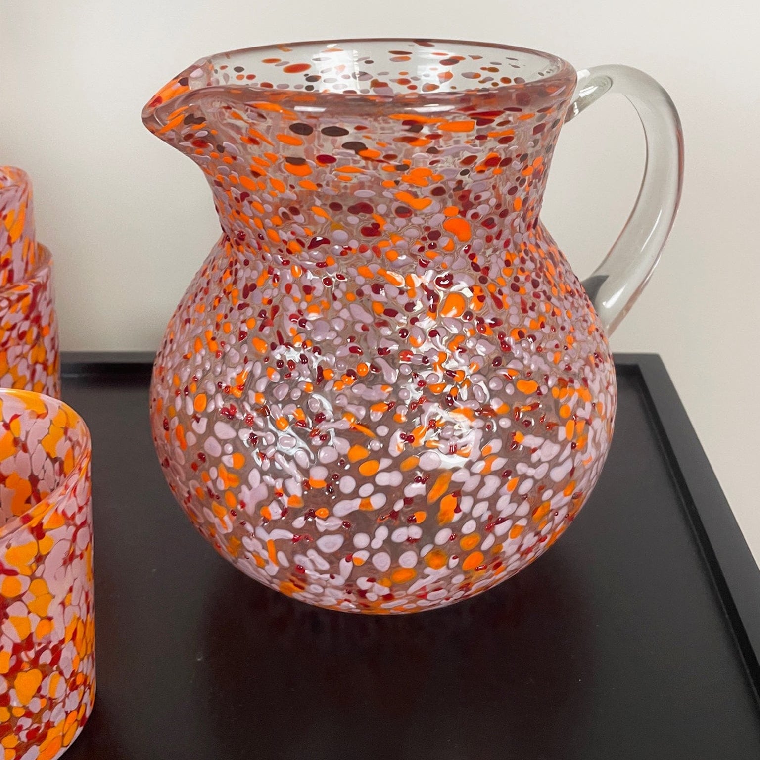 Glass pitcher with orange and pink speckled pattern on a dark surface
