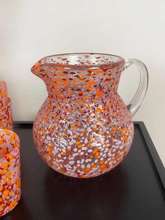 Glass pitcher with orange and pink speckled pattern on a dark surface