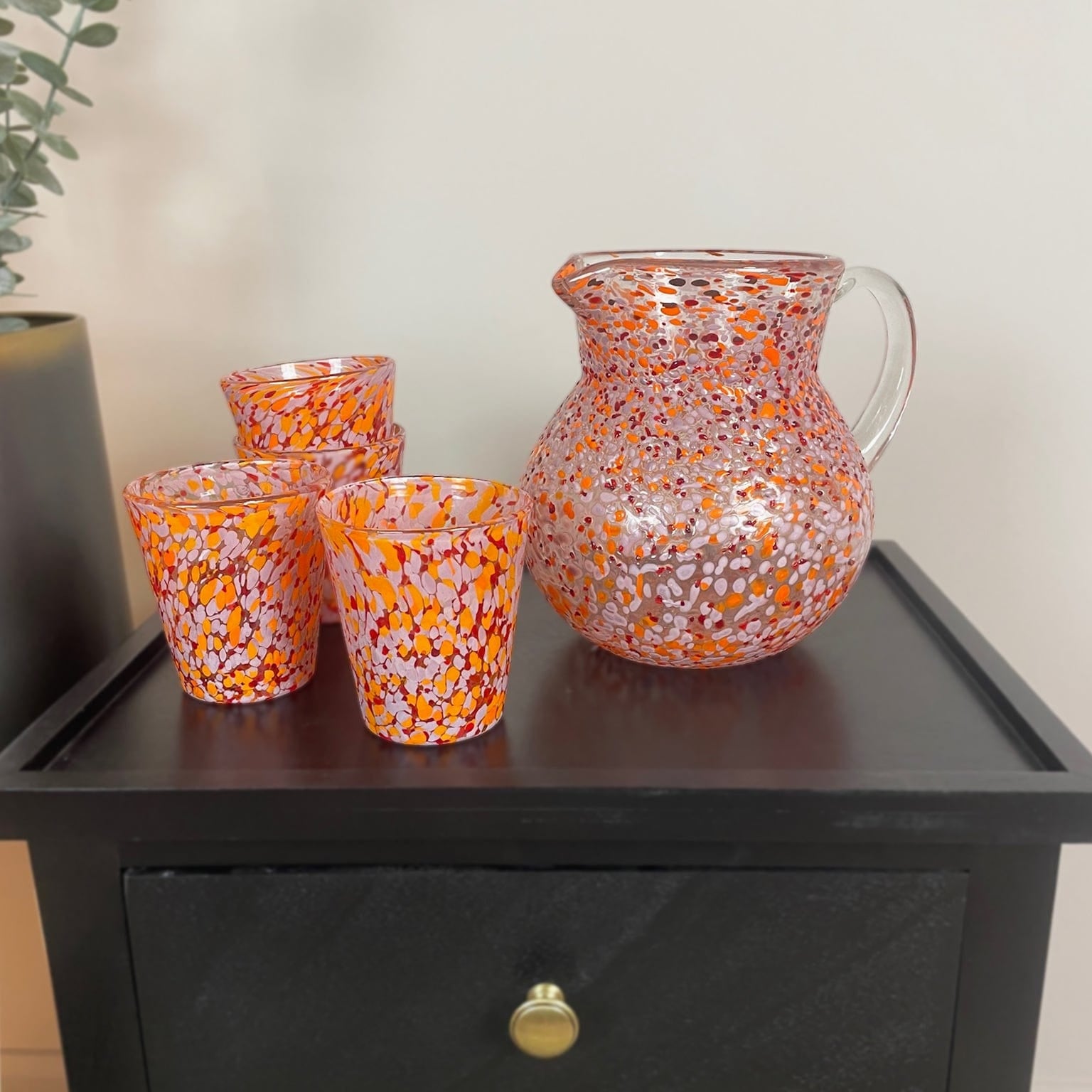 Set of colorful glassware on a dark wooden surface with a plant in the background