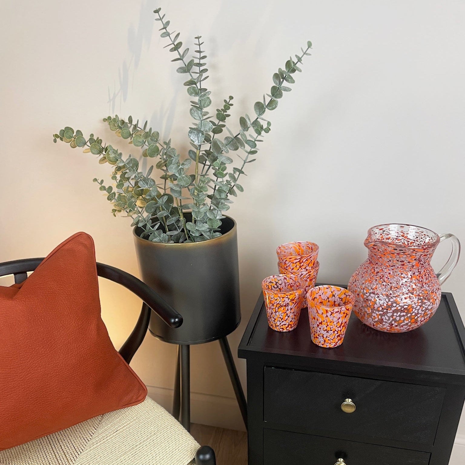 Black nightstand with decorative items next to a chair with an orange pillow
