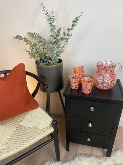 Black nightstand with decorative items next to a chair with an orange pillow