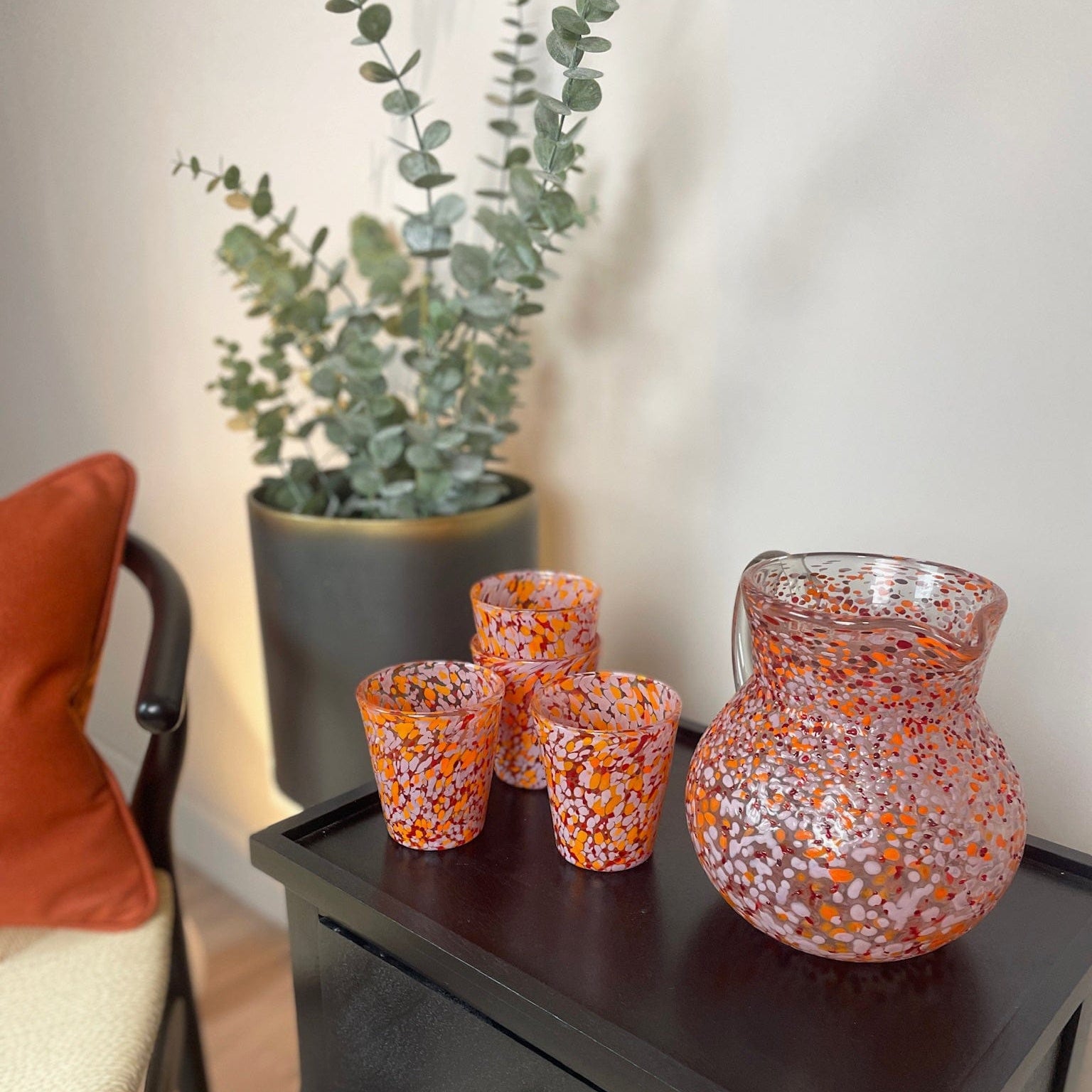 Decorative glass vases on a wooden side table with a plant in the background