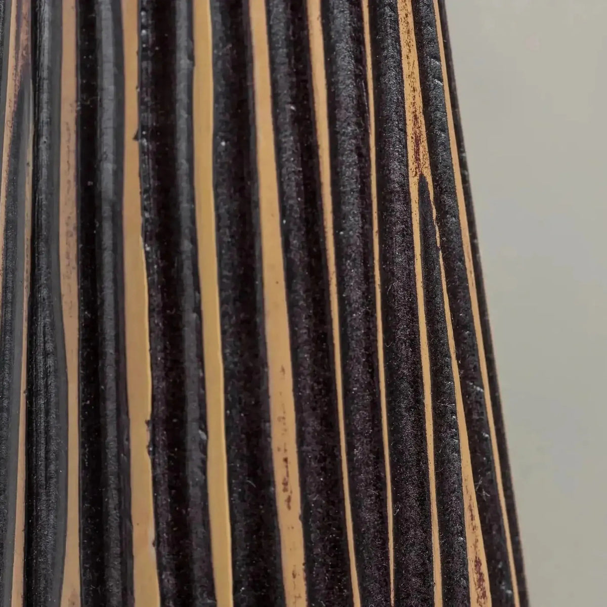 A close-up of a pleated fabric or curtain panel with alternating black and tan vertical stripes, set against a plain light gray background.