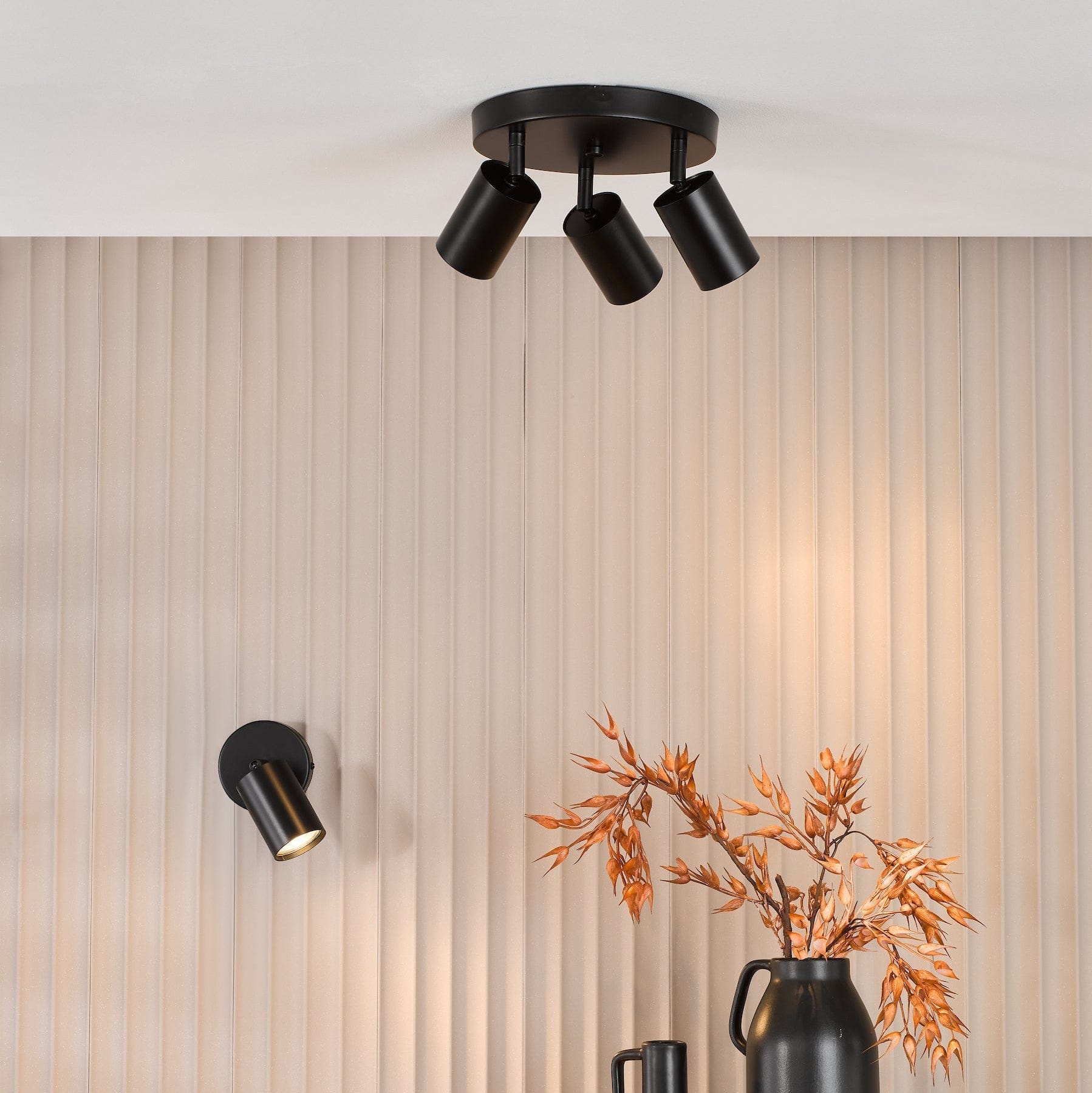 Modern ceiling light fixture on a neutral wall with decorative vases and branches.
