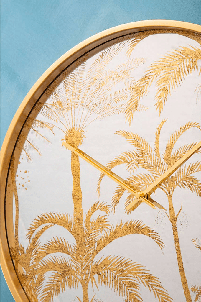 Decorative wall clock with gold palm tree design on a light background