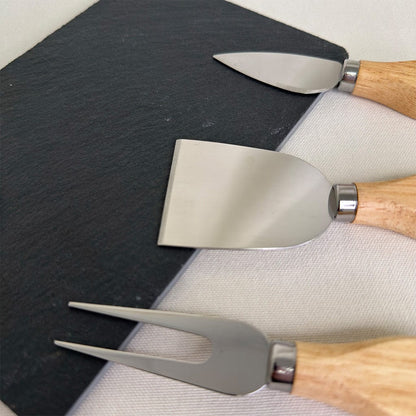 Set of three cheese tools with wooden handles on a slate board and white cloth.