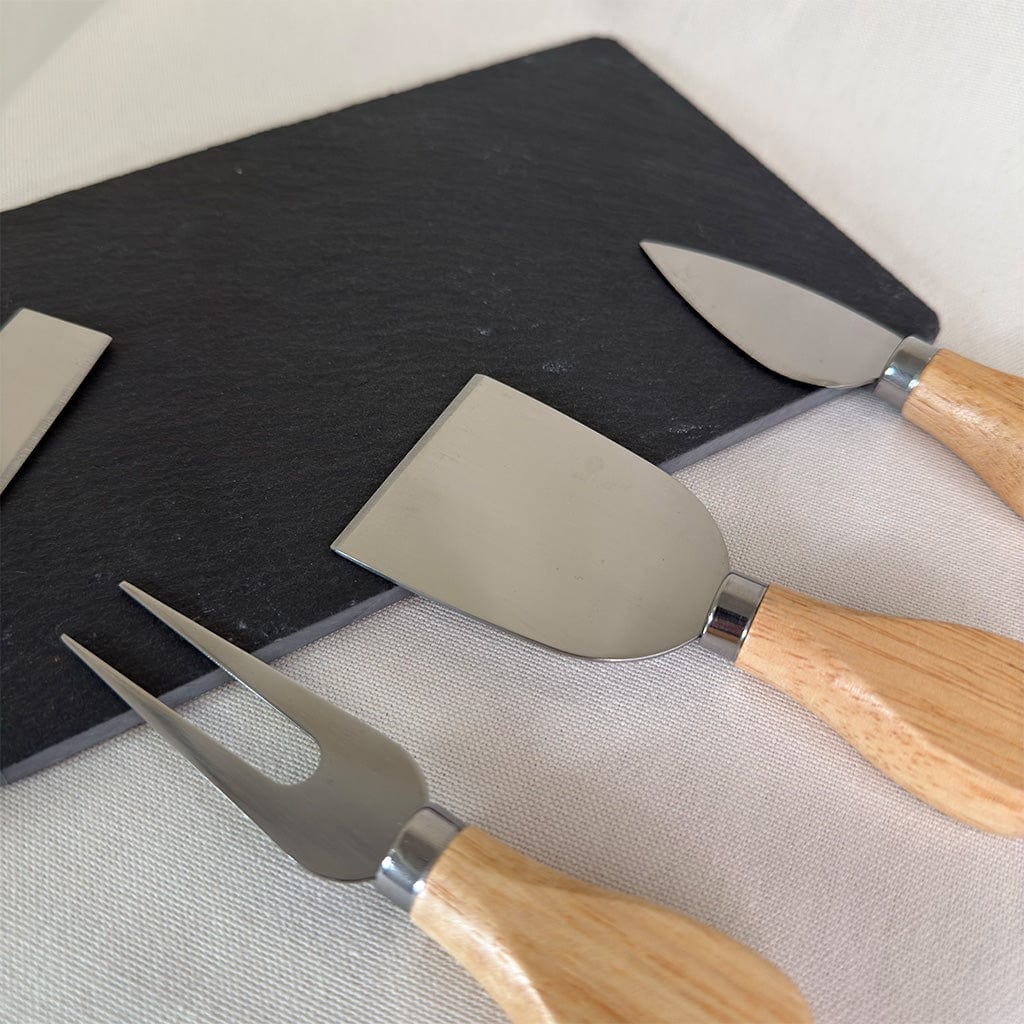 Set of cheese knives with wooden handles on a black cutting board.