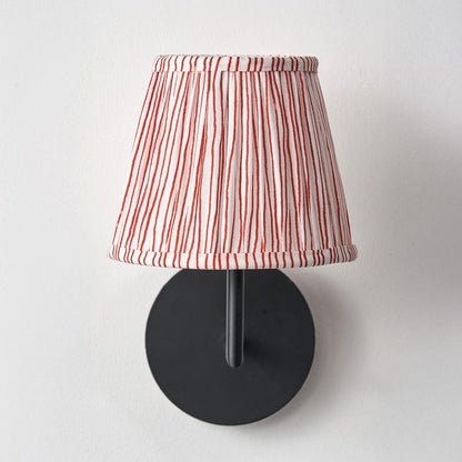 Wall-mounted lamp with a red and white striped shade on a light gray background