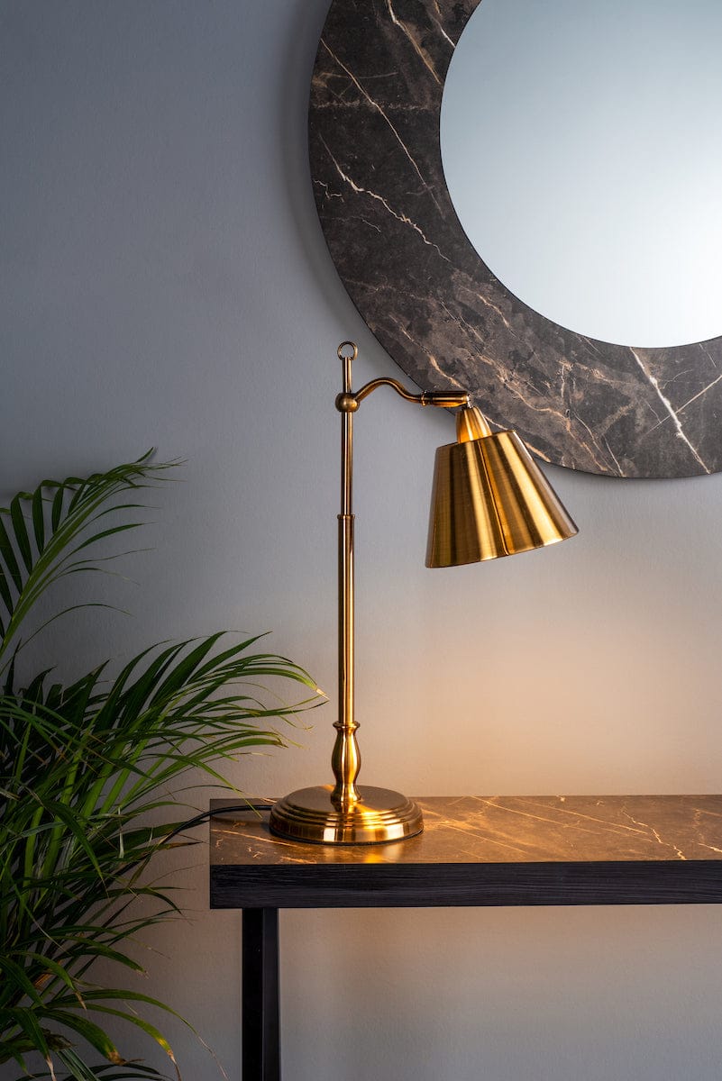 Gold table lamp on a marble surface with a decorative mirror in the background