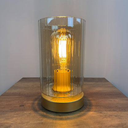 Decorative lamp with a glowing bulb inside a clear glass cover on a wooden surface.