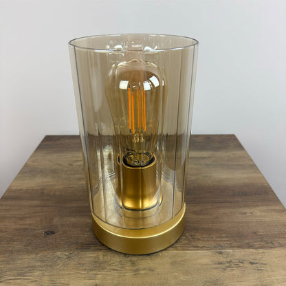 Decorative lamp with a amber glass shade and gold base on a wooden surface.