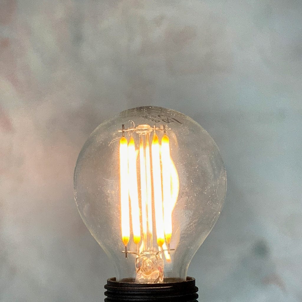 A clear, small Edison screw fitting LED golfball light bulb, lit against a marble background