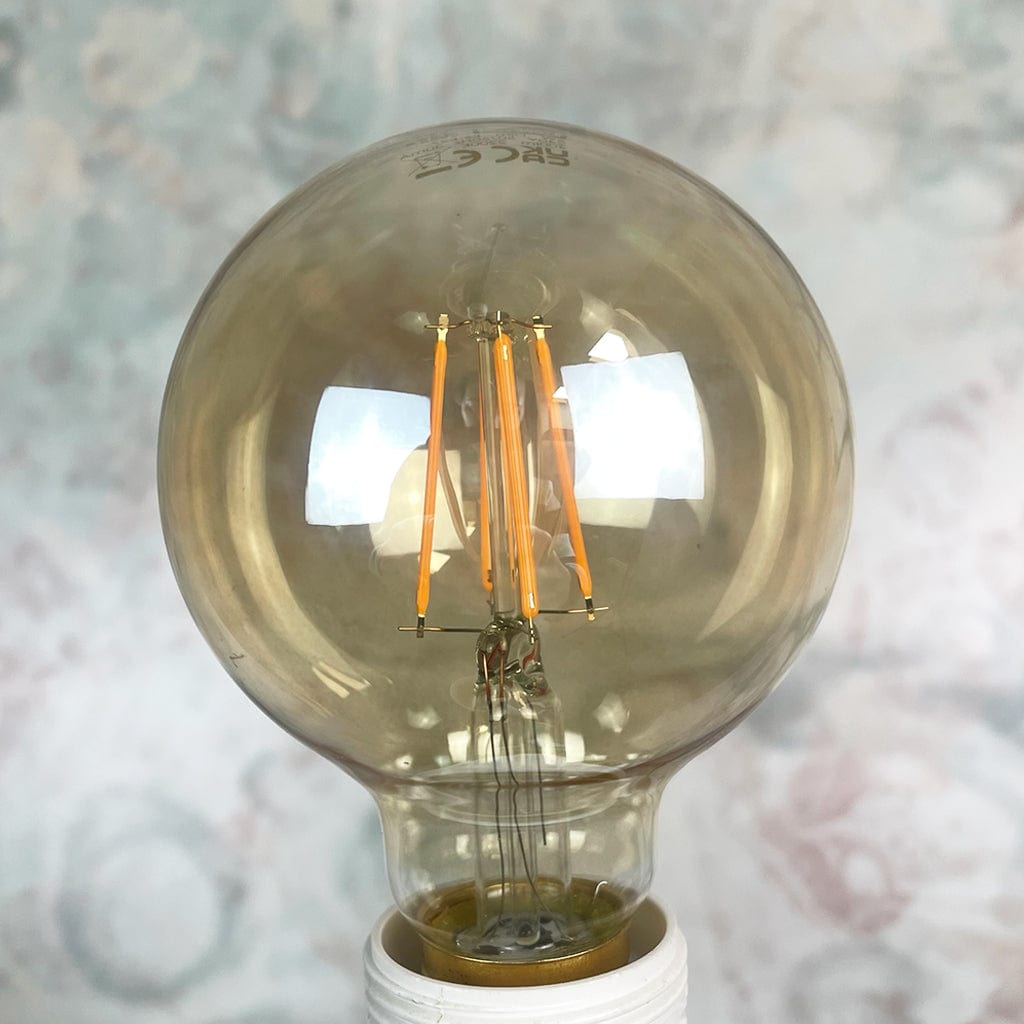An E27 amber-colored globe LED light bulb with a dimmable feature, displayed against a textured background.
