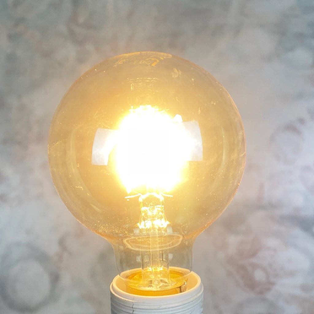 An E27 amber-colored globe LED light bulb with a dimmable feature, displayed against a textured background, lit.